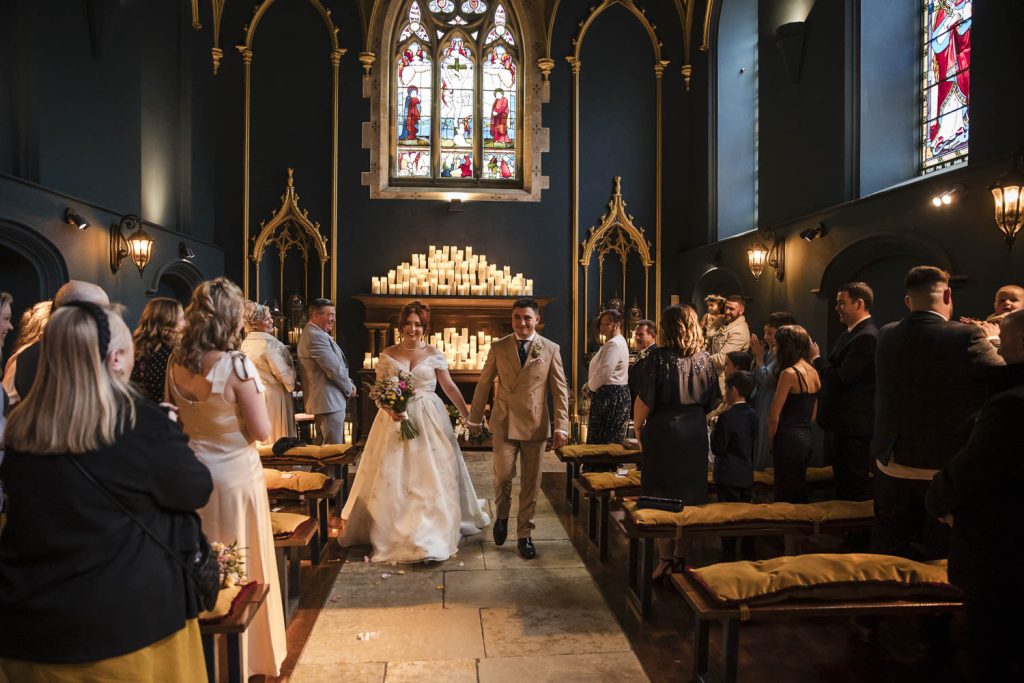 Bridal couple walk up the aisle of the church at Lartington Hall after getting married.
