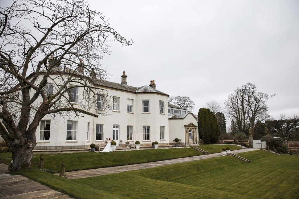 A photo of Lartington Hall with a bride and groom in the foreground on their wedding day.