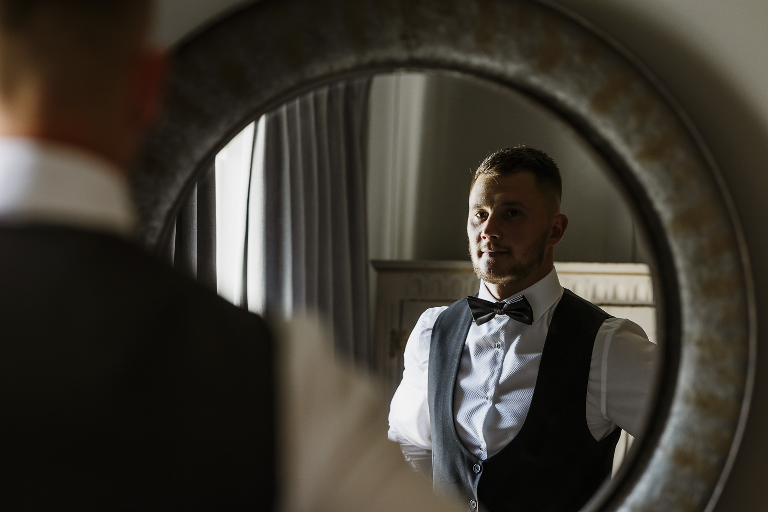 Groom getting ready in front of the mirror for his wedding at Le Petit Chateau.