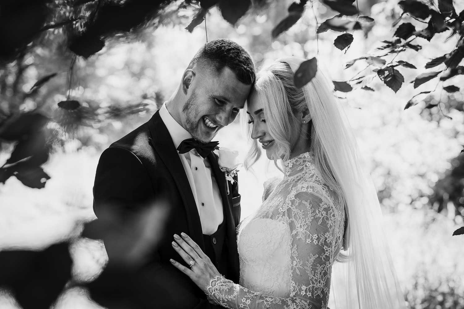 Bride and groom under a tree canopy embracing with the light shining through the leaves of the tree.