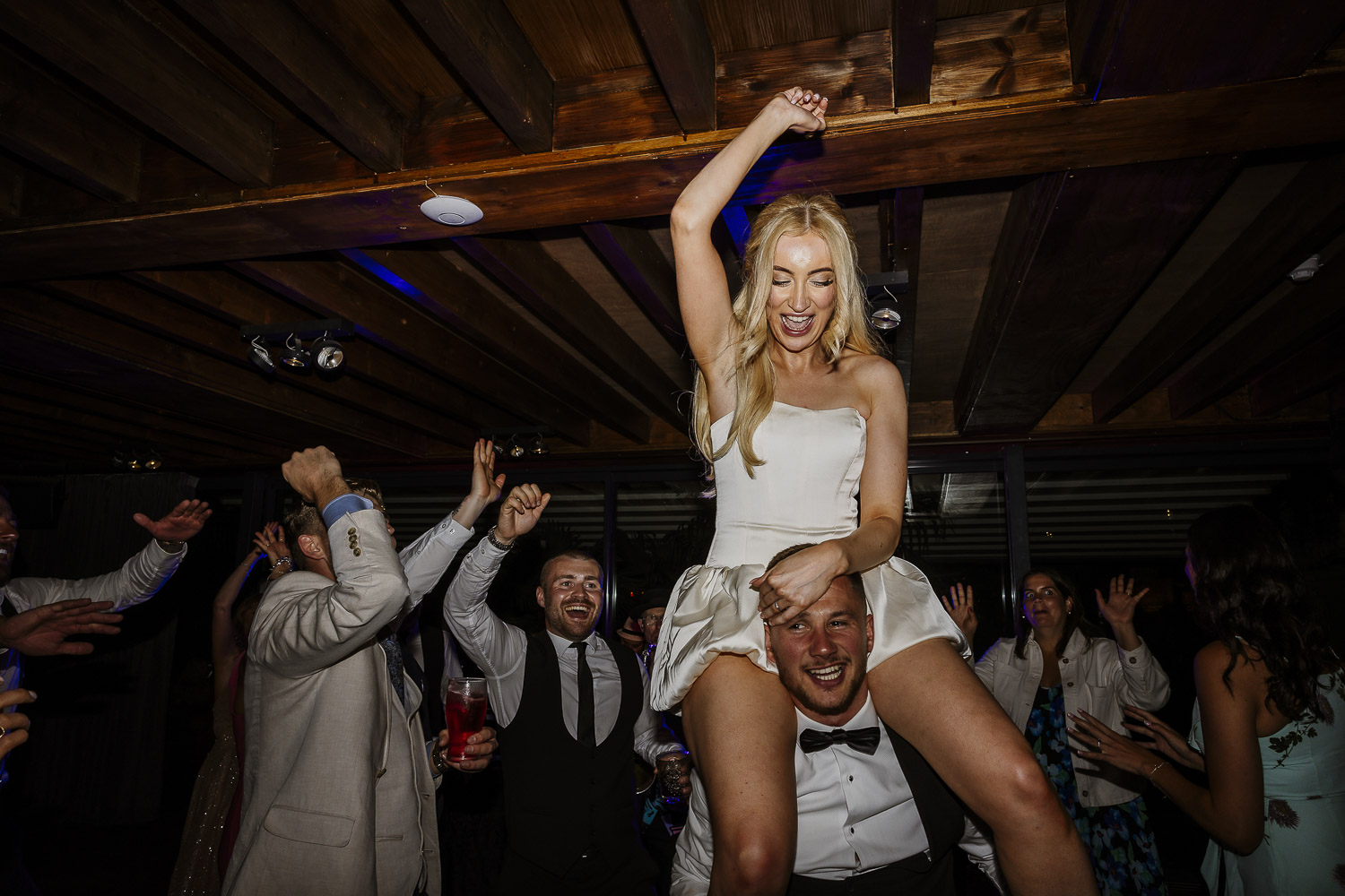 The bride on the shoulders of the groom on their wedding day, having a great time with a big smile on her face.