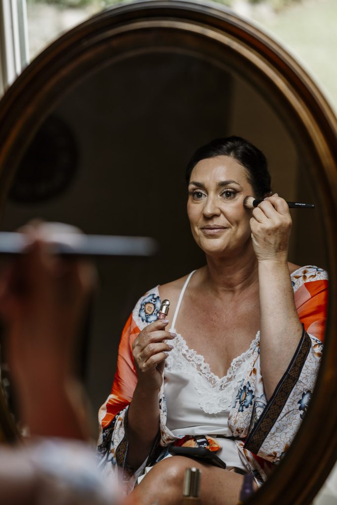 Bride doing her make up in a mirror getting ready for her wedding at Romignano wine farm