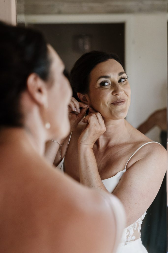 Bride putting in her earrings in a mirror.