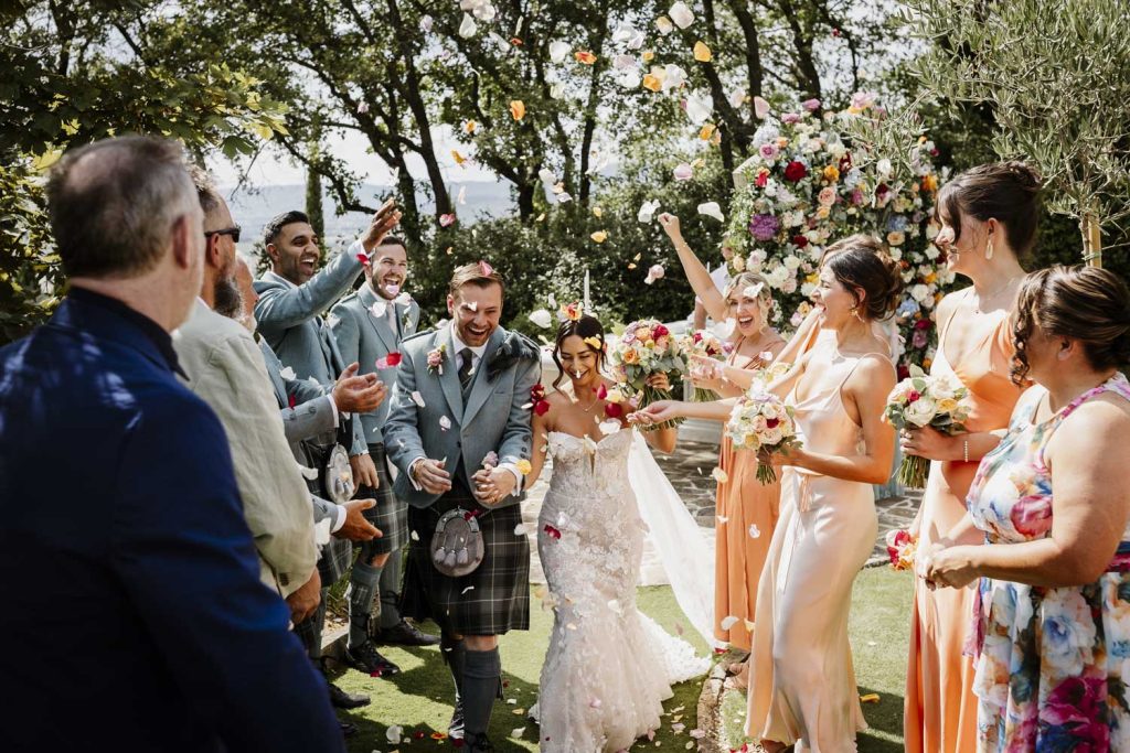 Bride and groom walking up the aisle with guests throwing confetti. Bride and groom look very happy and in love.