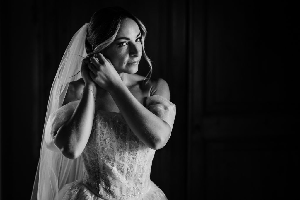 Bride in her wedding dress putting her earrings in
