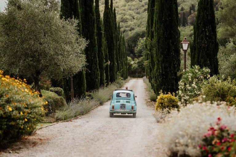 Bride and groom driving off in a vintage Fiat 500 on their wedding day